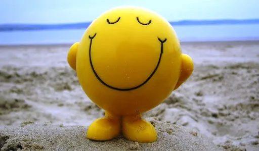 Boneco amarelo sorridente sentado na areia da praia