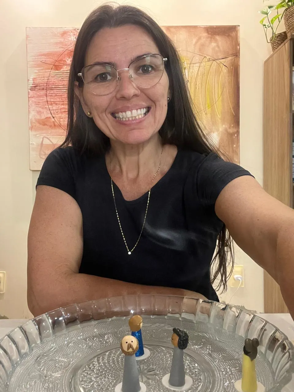 Elicéia Trindade sorrindo, sentada diante de uma mesa com os bonecos usados na constelação individual