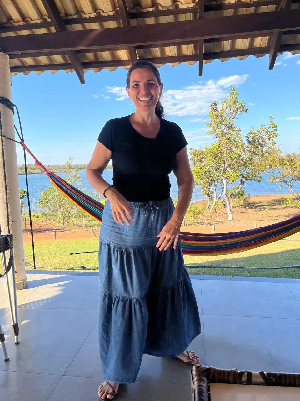 Elicéia Trindade em pé, sorrindo, em uma varanda com vista para o lago