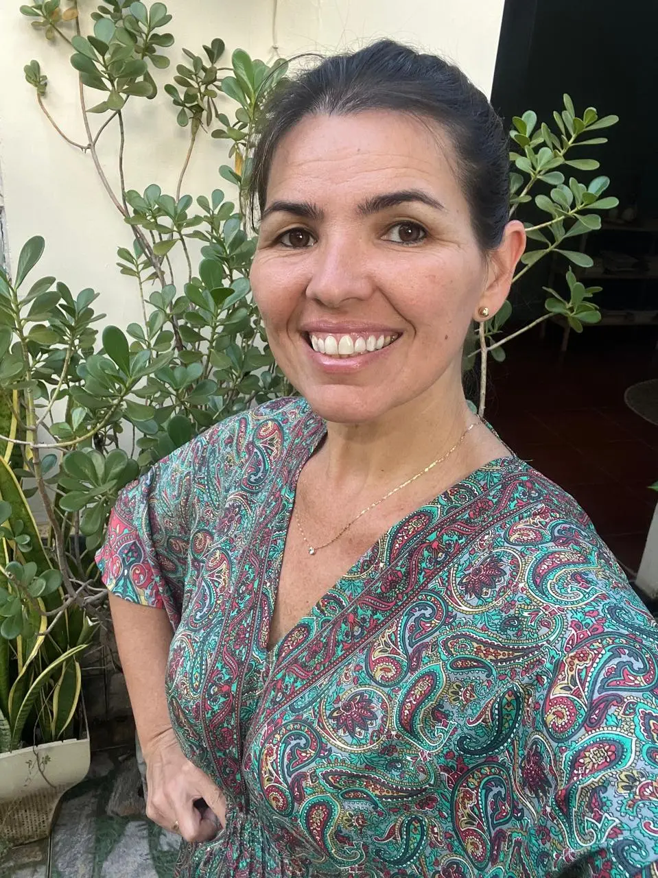 Elicéia Trindade sorrindo entre plantas, com blusa estampada em tons de verde